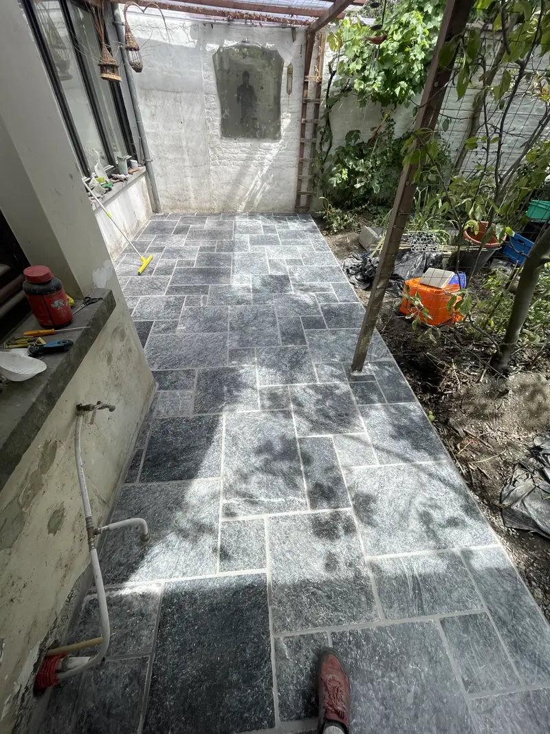 Terrasse en dalles de pierre bleue posées en appareil irrégulier, dans un jardin de ville étroit bordé de murs blancs